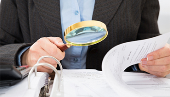 A professional woman in a suit uses a magnifying glass