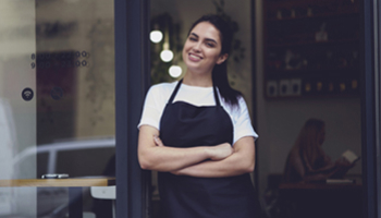 A woman wearing an apron stands outside a restaurant